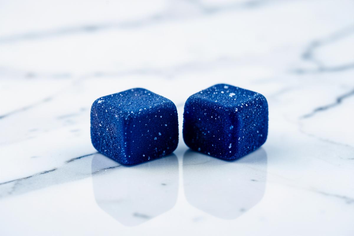 Two blue raspberry Love Bites gummies on a white marble surface